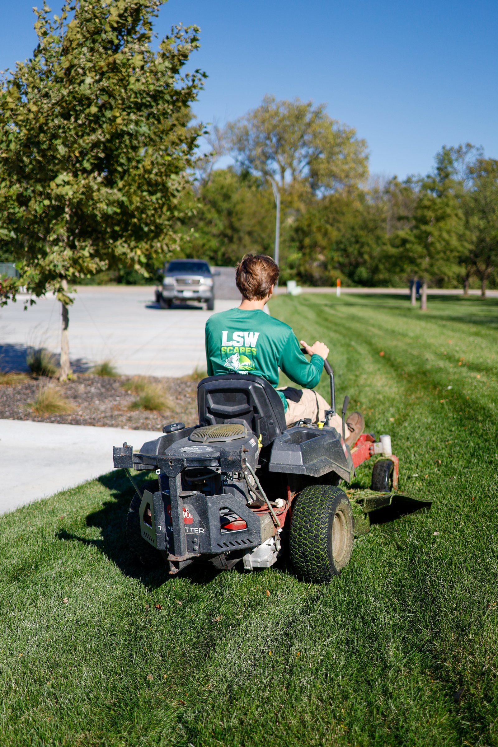 LSW Scapes mowing a striped lawn along a curb on a zero-turn mower